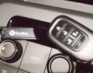 車のセンターコンソールに置かれたスマートキーとエネキー。黒いキーケースとエネキーが並び、背景にエアコン操作パネルが見える。