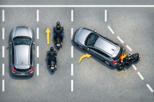 alt="上から見た道路で、停止した車の左側をバイクがすり抜け、車が左に寄せた瞬間に接触するまでの流れを4段階で示した横長の説明図。停止→すり抜け→左寄せ→接触の順に並び、事故の典型パターンを視覚的に理解できる構成。"