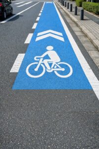 車道上に描かれた青い自転車ナビラインと白い矢印マーク。自転車の通行位置を示す道路表示で、車側の安全配慮義務を促す。